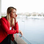 Female is contemplation looking over river with red top