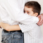 Close up of sad looking little boy hugging his dad.