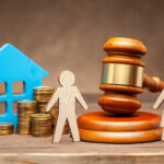 Male and female figures stood by pile of coins and cut out of a house depicting division of assets on divorce.