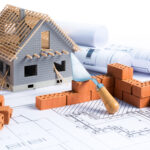 Model of new build home with bricks and trowel, sat on plans