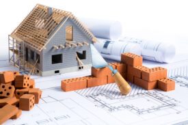 Model of new build home with bricks and trowel, sat on plans