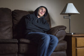 Teenage boy wearing a hoody sat on the sofa looking sad.