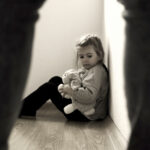 Scared little girl sitting in the corner with her teddy bear.