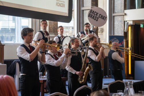 The Back Chat Brass band performing on stage at the Aspire Banking Hall.