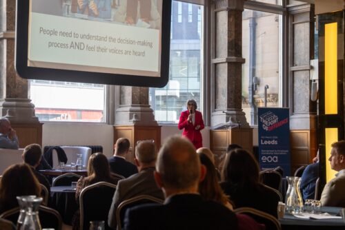 Noo Jones from Athena Professional speaking at the Aspire Banking Hall in front of a projector screen.