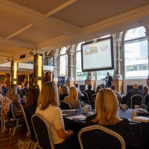 Robert Camp, conference chair, speaking at the Aspire Banking Hall in front of a projector screen.